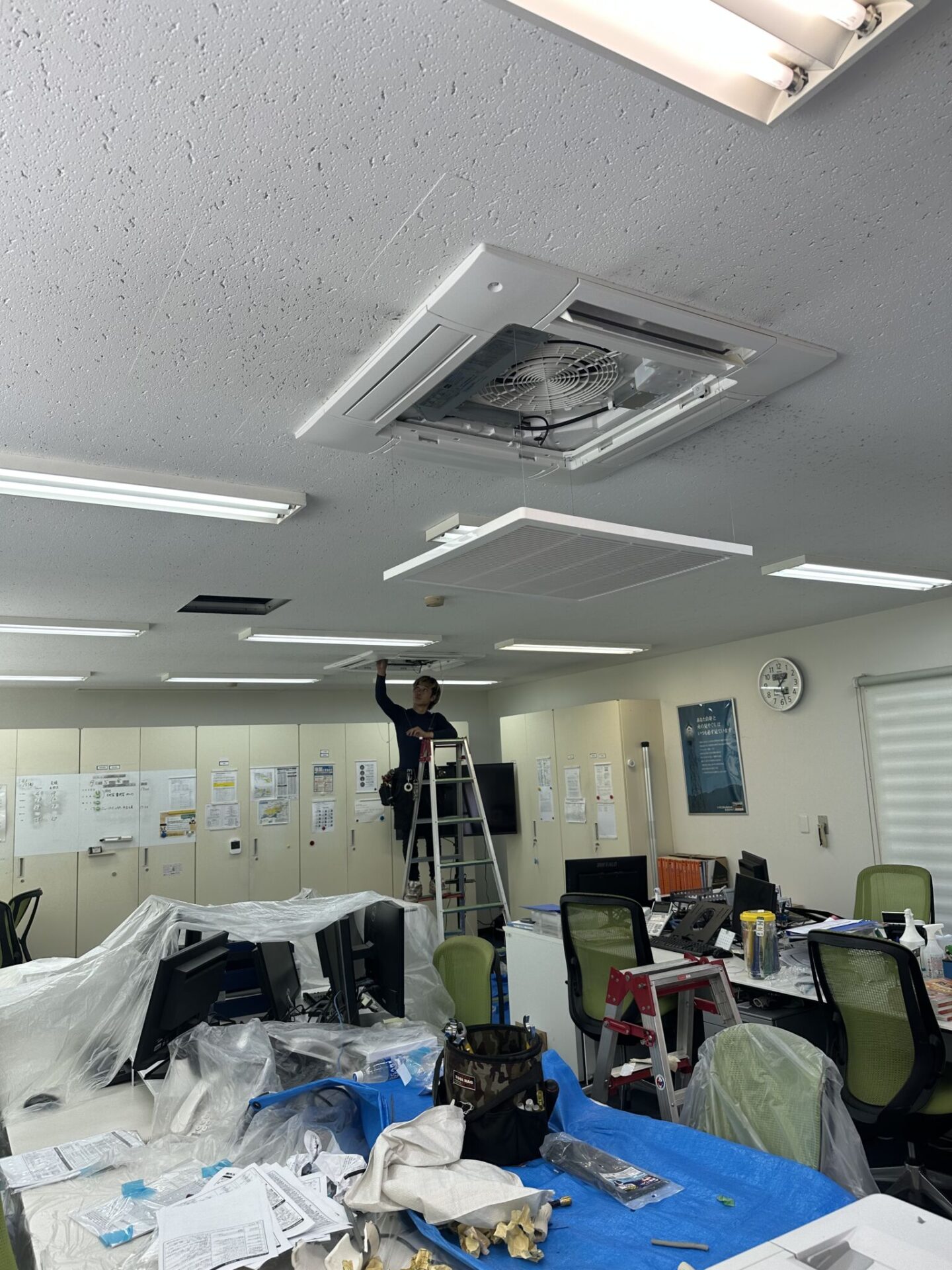 松山市のオフィスで天井カセット型エアコンの施工を行うスタッフ