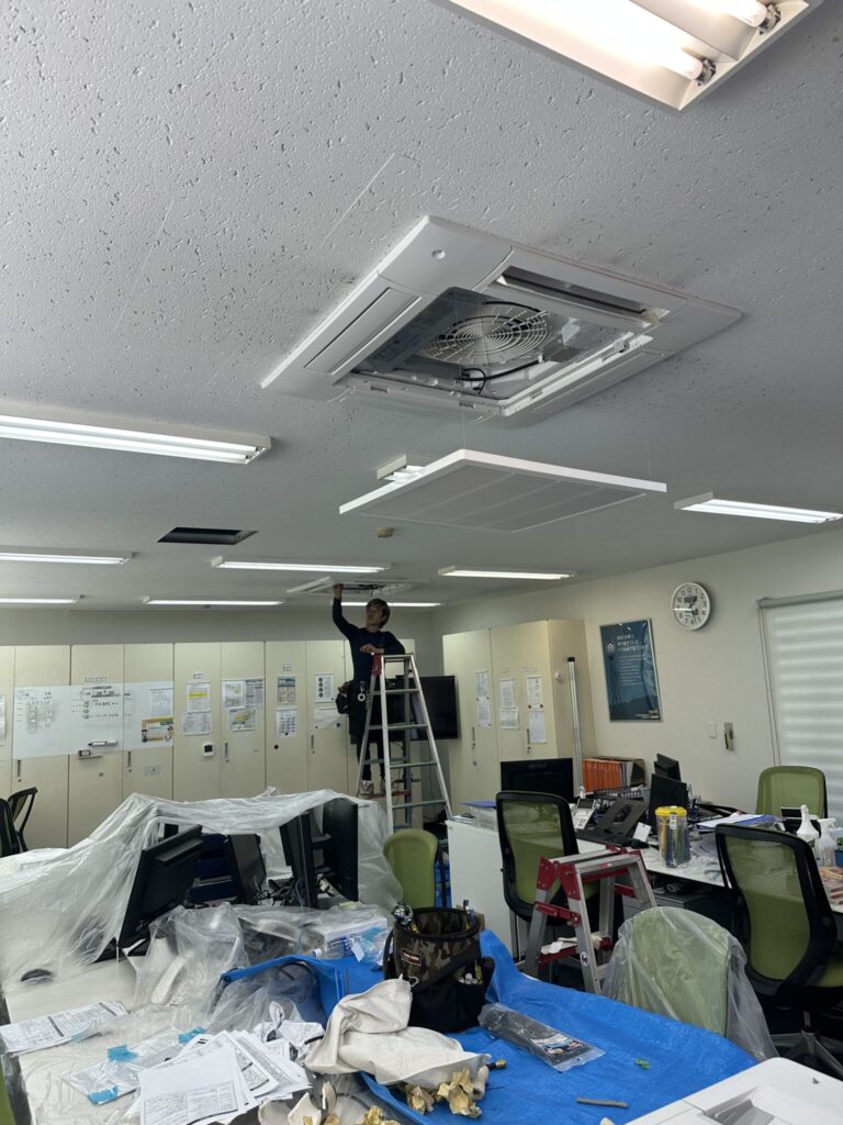 松山市のオフィスで天井カセット型エアコンの施工を行うスタッフ